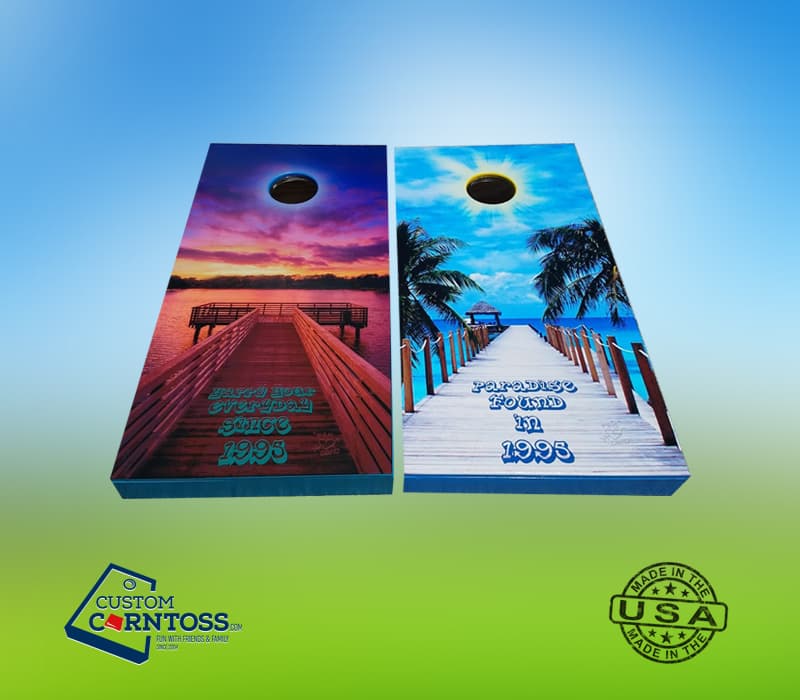 Full-wrap cornhole board decals printed with a sunset dock photo and a tropical beach dock photo